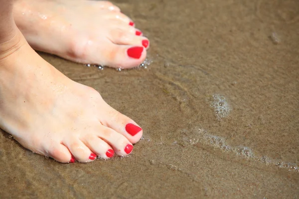 Pies de mujer con pedicura roja relajándose sobre arena — Foto de Stock