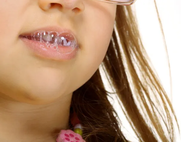 Close up little girl in glasses doing fun saliva bubbles — Stock Photo, Image