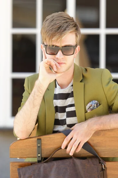 Junger schöner Mann sitzt auf Bank — Stockfoto