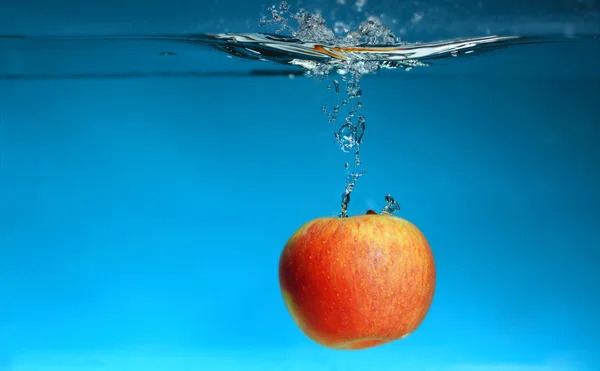 Gult äpple i vattnet stänk över blått — Stockfoto