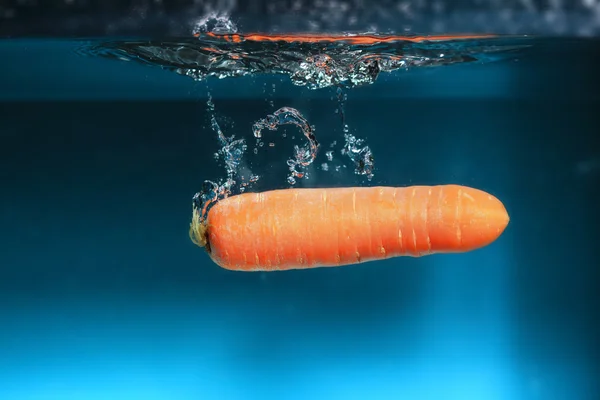 Zanahoria en el agua salpica sobre azul —  Fotos de Stock