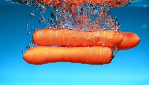 Zanahoria en el agua salpica sobre azul — Foto de Stock