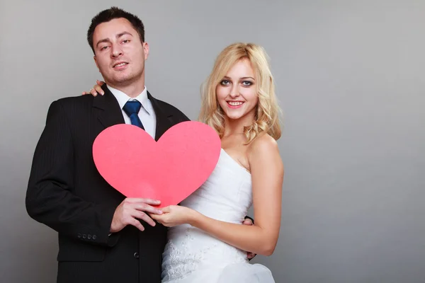 Портрет счастливой невесты и жениха с красным сердцем на сером — стоковое фото
