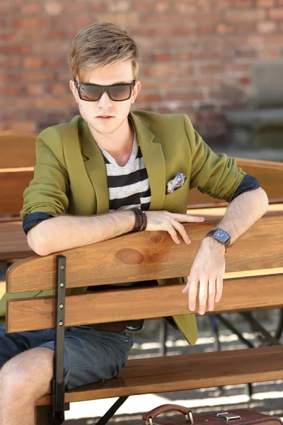 Young handsome man with suitcase waits on bench — Stock Photo, Image