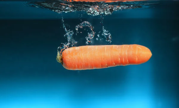 Carota nell'acqua spruzzata sopra il blu — Foto Stock