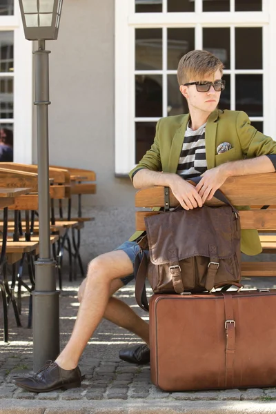 Young handsome man with suitcase waits on bench — Stock Photo, Image