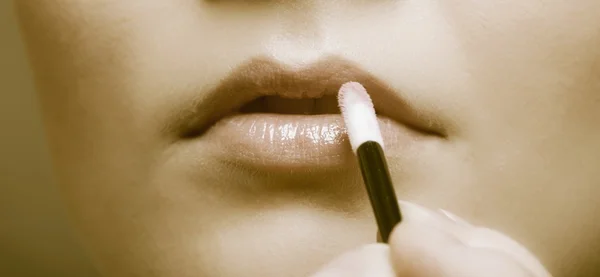 Makeup. Girl applying lipgloss lipstick on lips. Part of face. Sepia. — Stock Photo, Image