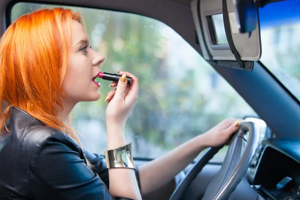 Mulher motorista pintar os lábios enquanto dirige um carro — Fotografia de Stock