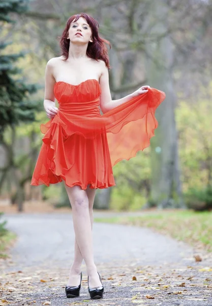 Full length fashionable woman in vibrant red dress in park — Stock Photo, Image