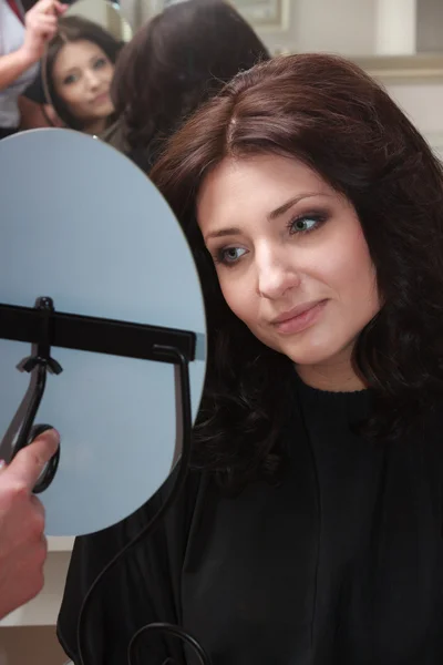Aynaya bakarak yeni saç modeli ile esmer kadın. Kuaför Salonu. — Stok fotoğraf