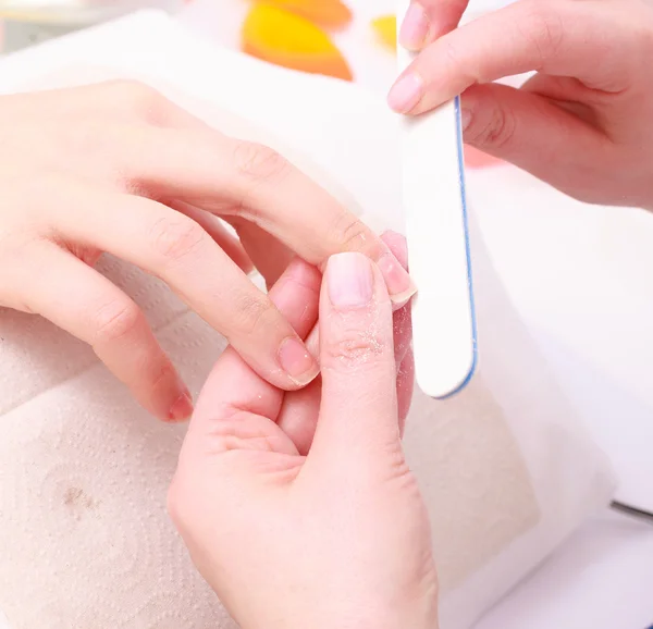 Beautician with file filing nails female client. Woman spa beauty salon