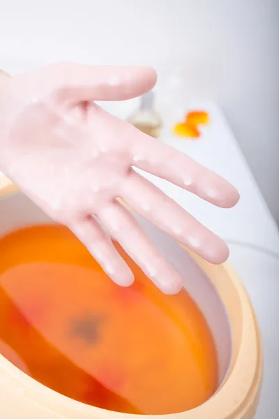 Vrouwelijke hand oranje parrafin wax in kom. manicure-beautysalon spa — Stockfoto