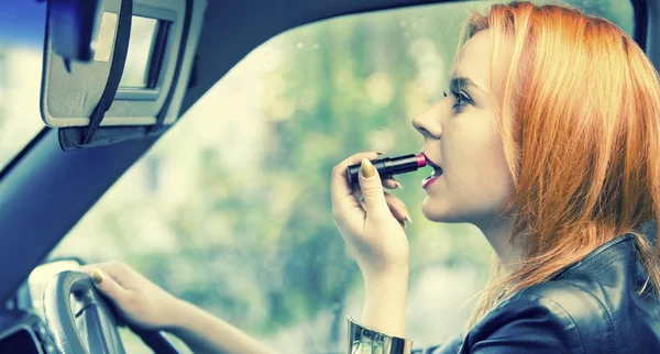 Czerwonych włosach kobiety stosowania szminki na usta w samochodzie. niebezpieczeństwo na drodze. — Zdjęcie stockowe