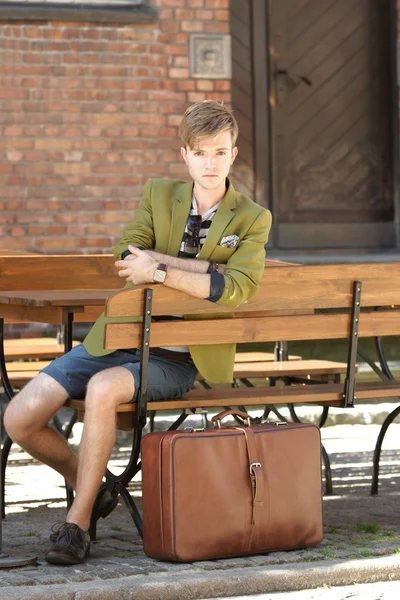 Joven hombre guapo con maleta espera en el banco — Foto de Stock