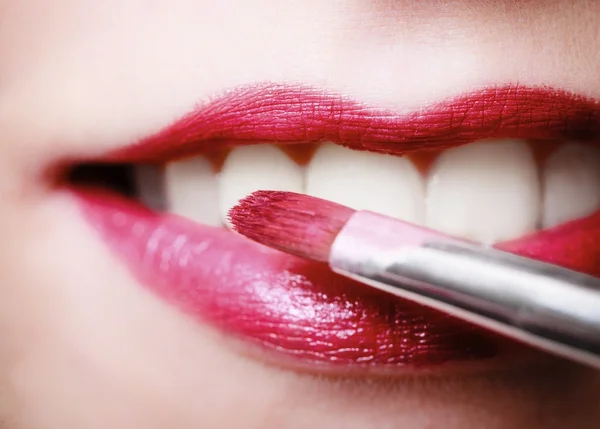 Closeup vrouwelijke rood roze lippen met make-up lippenstift borstel — Stockfoto