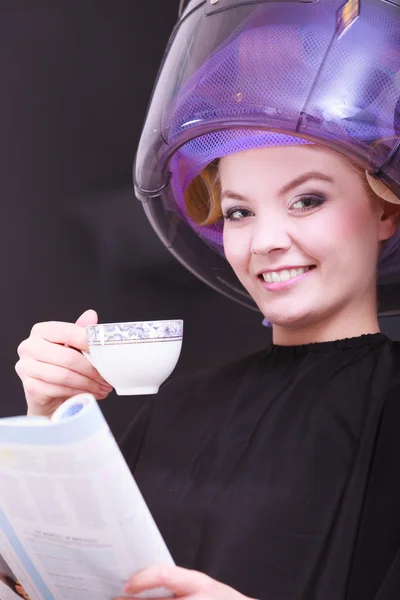 Chica leyendo la revista bebiendo café. Secador de pelo en peluquería — Foto de Stock