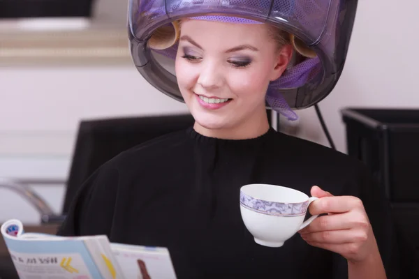 Chica leyendo la revista bebiendo café. Secador de pelo en peluquería — Foto de Stock