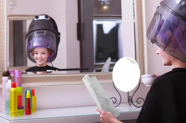 Chica leyendo la revista bebiendo café. Secador de pelo en peluquería —  Fotos de Stock