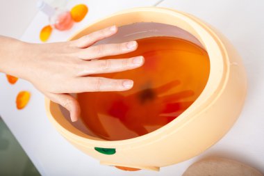 Female hand and orange paraffin wax bowl. Woman in beauty salon clipart