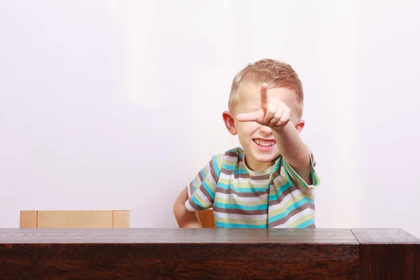 Porträt eines glücklichen blonden Jungen, der auf dich am Tisch zeigt — Stockfoto