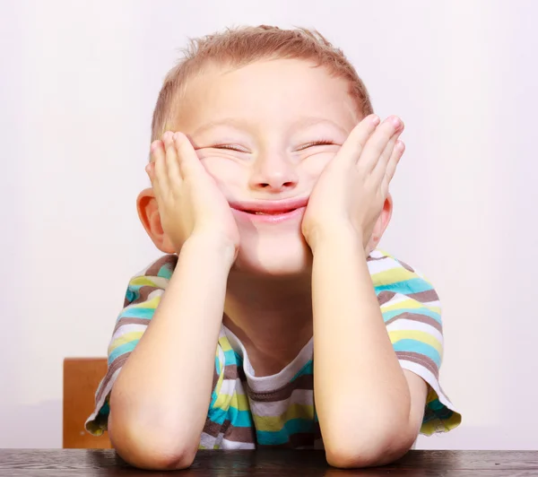 Portret blond chłopiec dziecko co śmieszne twarz przy stole — Zdjęcie stockowe