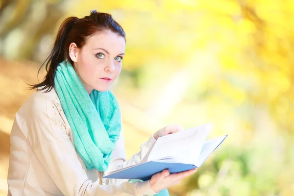 Молодая девушка отдыхает в осеннем парке, читая книгу — стоковое фото