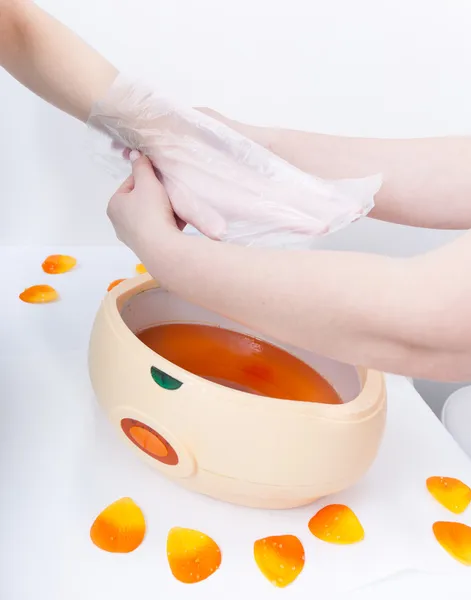 Cera de parrafina naranja de mano femenina en tazón. Salón de belleza de manicura spa —  Fotos de Stock