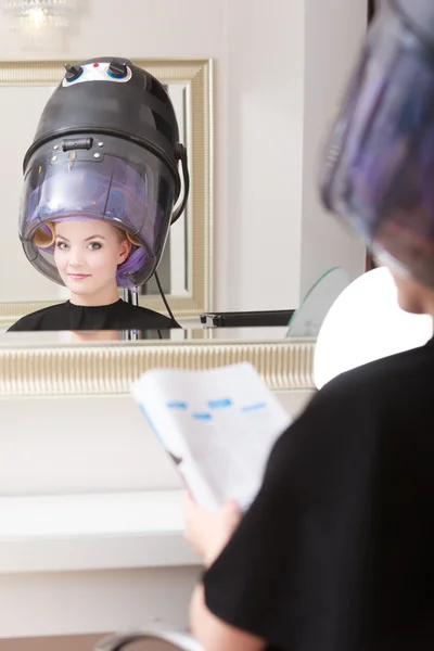 Mujer cliente rulos en pelo lee revista peluquería salón de belleza. — Foto de Stock