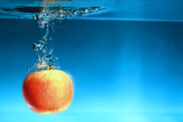 Manzana amarilla en el agua salpica sobre azul —  Fotos de Stock