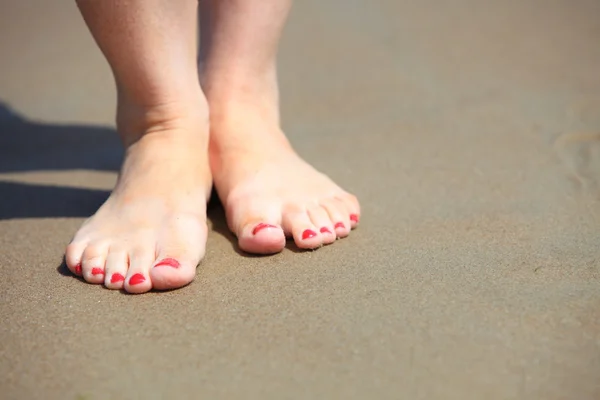 Frauenfüße mit roter Pediküre entspannen auf Sand — Stockfoto