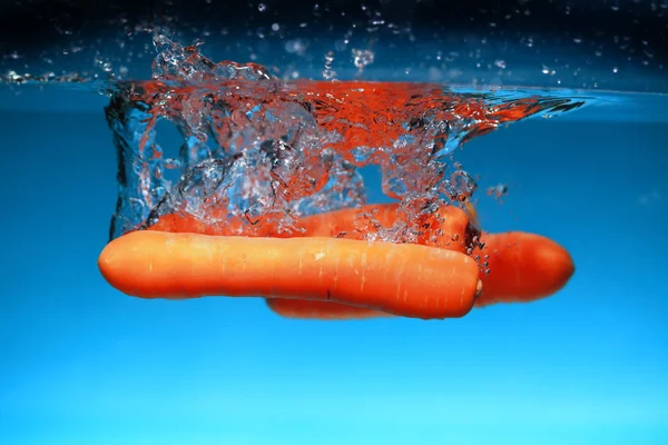 Cenoura no respingo de água sobre azul — Fotografia de Stock