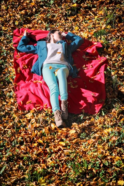 Genç kızın rahatlatıcı sonbahar Park kırmızı battaniye var yalan — Stok fotoğraf