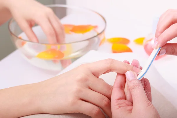 Beautician with file filing nails female client. Woman spa beauty salon