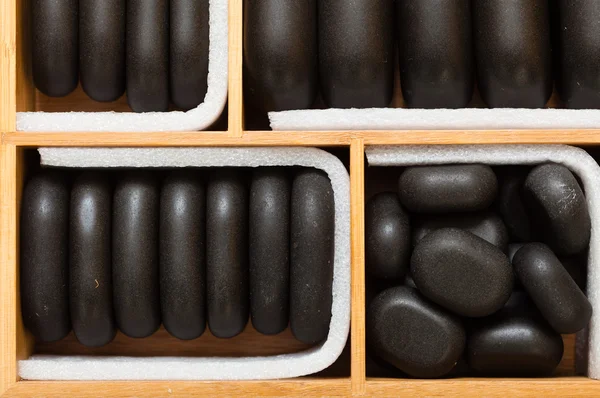 Schwarze Wellness-Zen-Massagesteine im Holzetui als Hintergrund — Stockfoto