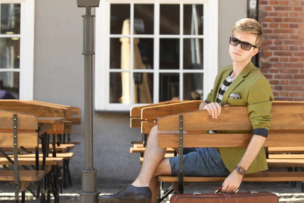 Young handsome man with suitcase waits on bench — Stock Photo, Image