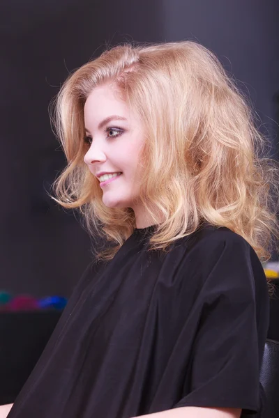 Menina sorridente bonita com cabelo ondulado loiro no salão de beleza de cabeleireiro — Fotografia de Stock