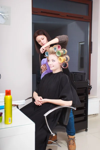 Femme dans un salon de beauté. Fille blonde avec des boucles de cheveux rouleaux par coiffeur. Coiffure . — Photo