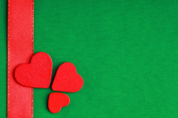 Κόκκινο ξύλινα διακοσμητικά καρδιές σε φόντο πράσινο ύφασμα — Φωτογραφία Αρχείου