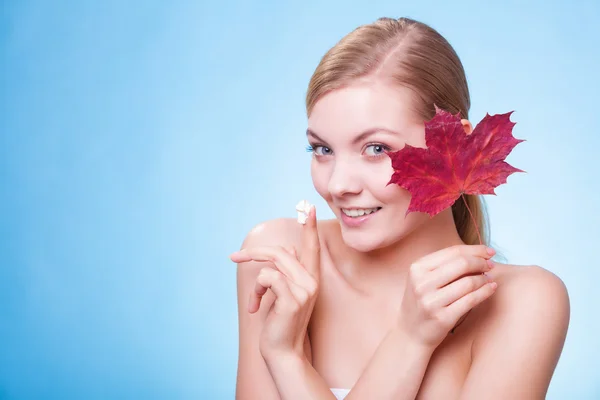 Huidverzorging. Gezicht van jonge vrouw meisje met rode esdoorn blad. — Stockfoto