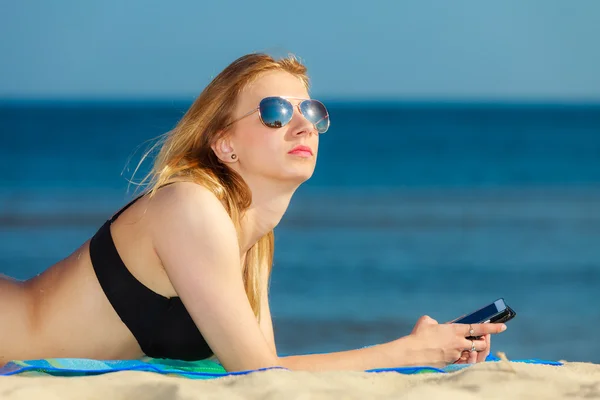 Sommar semester Flicka med telefon garvning på stranden — Stockfoto