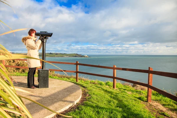 Mujer mirando a través de prismáticos turísticos con vistas al océano —  Fotos de Stock