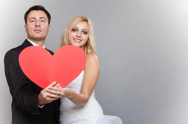 Porträt glücklicher Braut und Bräutigam mit rotem Herz auf grau — Stockfoto
