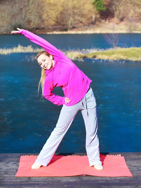 Woman teenage girl in tracksuit doing exercise on pier outdoor — Stock Photo, Image