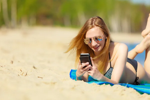 Sommar semester Flicka med telefon garvning på stranden — Stockfoto