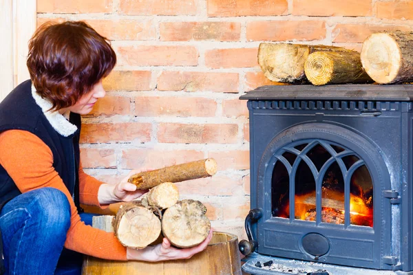 Woman putting some more wood on fireplace. Heating. — Stock Photo, Image