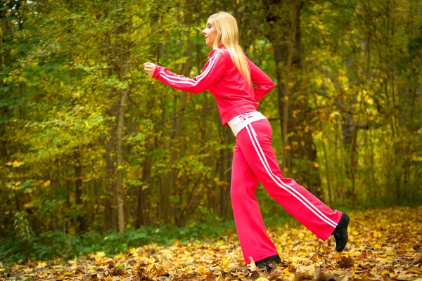 Blonde girl young woman running jogging in autumn fall forest park — Stock Photo, Image