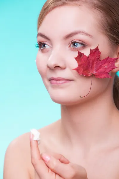 Huidverzorging. Gezicht van jonge vrouw meisje met rode esdoorn blad. — Stockfoto