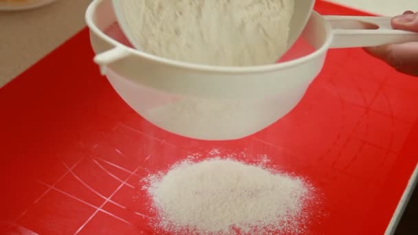 Mãos femininas de dona de casa ou chef derramando farinha ingrediente da massa na peneira no tabuleiro de pastelaria — Vídeo de Stock
