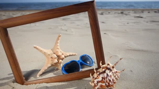 Shell, Starfish and glasses in wooden frame on Beach — Stock Video