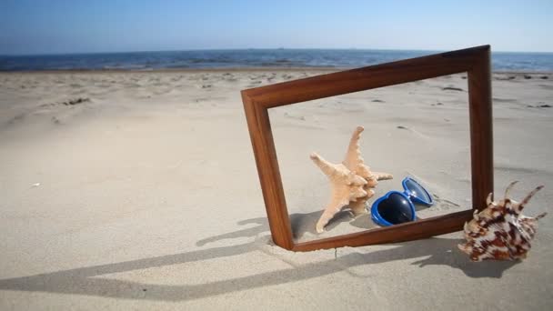 Concha, estrella de mar y gafas en marco de madera en la playa — Vídeos de Stock